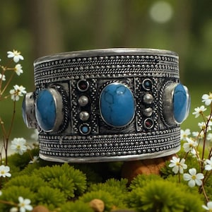 Può includere: Un ampio bracciale a polsino in argento con pietre ovali turchesi e un'intricata lavorazione del metallo. Il bracciale presenta una serie di pietre turchesi incastonate in cornici individuali, intervallate da elementi decorativi più piccoli. Il bracciale è largo circa 5 cm.