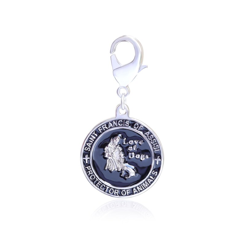 Puede incluir: Un dije plateado con un cierre de mosquet&oacute;n. El colgante circular presenta el texto "San Francisco de As&iacute;s, Protector de los Animales" y una imagen de San Francisco con un perro. El colgante es negro y plateado.