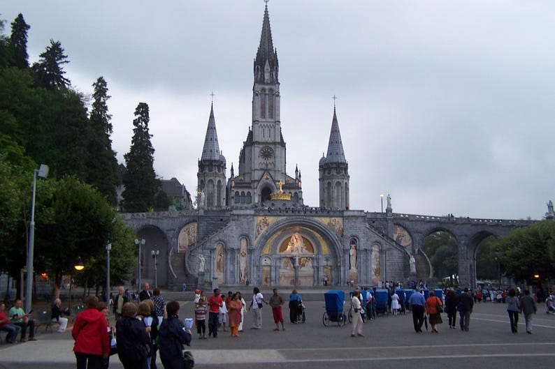 Puede incluir: Una gran catedral ornamentada con m&uacute;ltiples agujas y una fachada detallada. El edificio es de piedra gris, con pasarelas arqueadas y una gran plaza delante. La gente camina por la plaza.