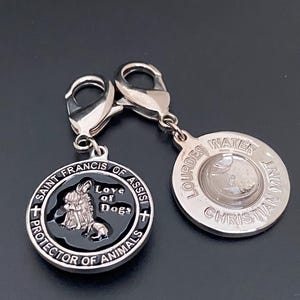 Puede incluir: Dos colgantes plateados con forma de perro. Un colgante presenta el texto "San Francisco de As&iacute;s, Protector de Animales, Amor de Perros". El otro colgante tiene el texto "Lourdes Water Christian Mint."