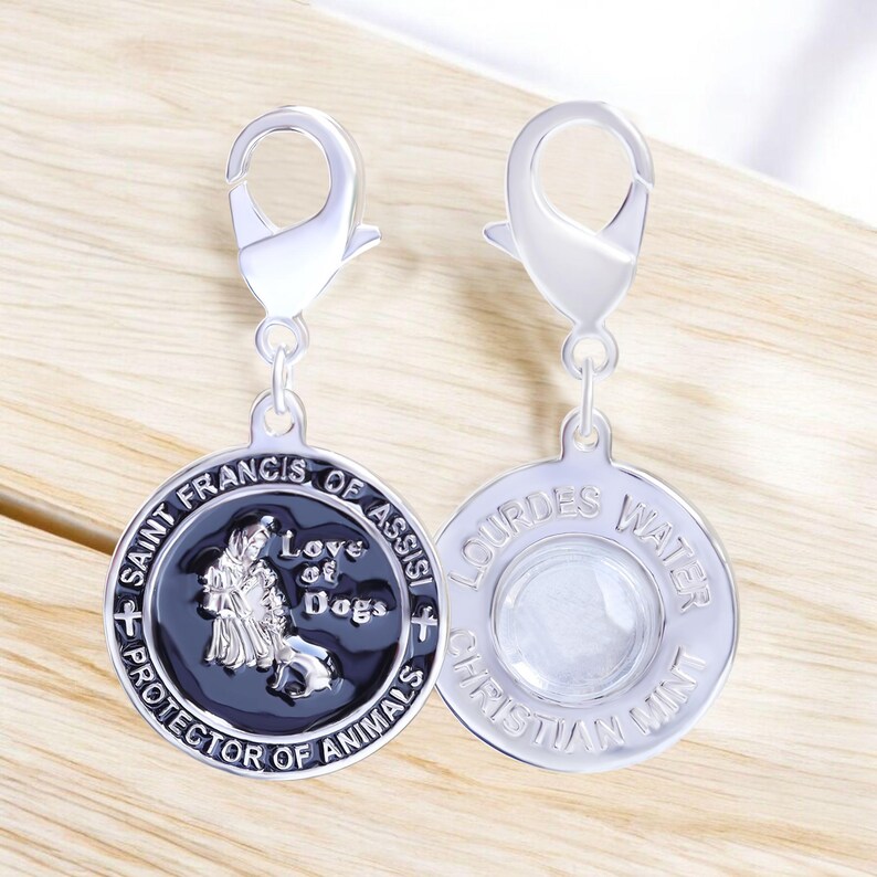 Puede incluir: Dos colgantes plateados para perros con cierres de mosquet&oacute;n. Un colgante presenta a San Francisco de As&iacute;s con el texto "Love of Dogs" y "Protector of Animals". El otro colgante tiene "Lourdes Water" y "Christian Mint".
