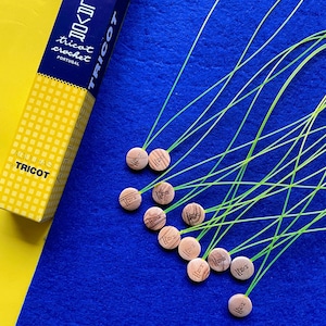 May include: A close-up of a blue surface with green yarn and wooden circular tags with the word "Tricot" printed on them. The tags are attached to the yarn with knots.