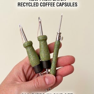 Könnte beinhalten: Drei Punch-Needles mit strukturierten grünen Griffen aus recycelten Kaffeekapseln. Die Nadeln haben Metallspitzen und eine silberne Einstellschraube am rechten Werkzeug. Text: NEW FROM LAVOR RECYCLED COFFEE CAPSULES ALL SIZES IN ONE SET.