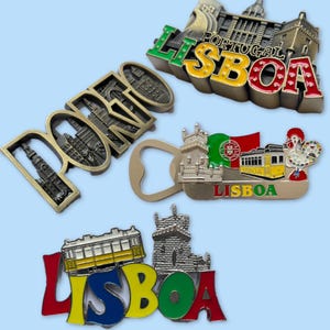 Op de afbeelding: Een verzameling souvenirmagneten en een flesopener met de steden Lissabon en Porto, Portugal. De magneten tonen de stadsnamen en bezienswaardigheden in verschillende kleuren, waaronder rood, geel, groen en brons. De flesopener heeft een zilveren afwerking.