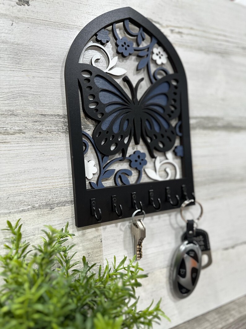 May include: Black wooden key holder with a blue and white butterfly design. The holder has six hooks for hanging keys.