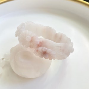 May include: A white jade bangle with a carved floral design. The bangle is decorated with delicate pink flowers and leaves.