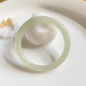 May include: A light green jade bangle bracelet. The bracelet is smooth and polished, and it has a simple, elegant design.