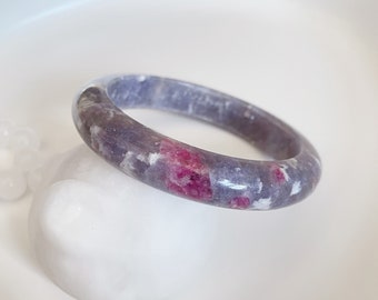 May include: A purple and white bangle bracelet with pink and white flecks throughout. The bracelet is made of polished stone.