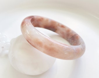 May include: A pink and white agate bangle bracelet with a smooth, polished finish. The bracelet is made of natural stone and has a unique, swirling pattern.