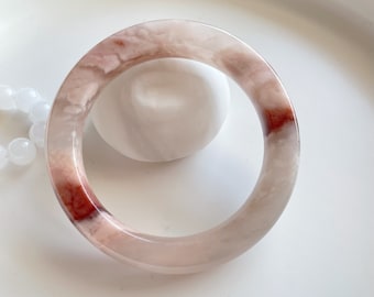 May include: A translucent pink and white bangle bracelet with a red swirl design.