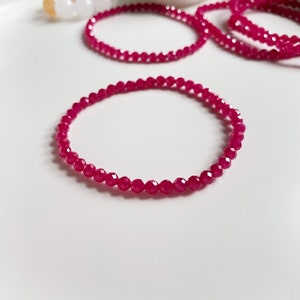 May include: A pink gemstone bracelet made of small, faceted beads. The bracelet is on a white surface.