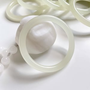 May include: A set of pale green jade bangle bracelets. The bracelets are smooth and polished, and they are stacked on top of each other.