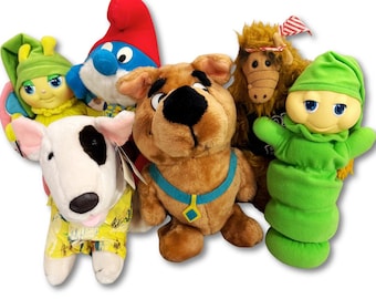 May include: A collection of plush toys featuring cartoon characters. Includes a brown Scooby-Doo, a white and black dog, a green caterpillar, a Smurf, an ALF doll, and a yellow and green doll with wings.