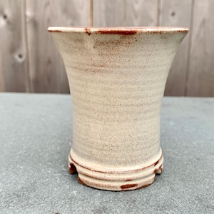 May include: A white ceramic planter with a red rim and a textured surface. The planter has a flared opening and a rounded base.