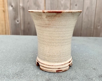 May include: A white ceramic planter with a red rim and a textured surface. The planter has a flared opening and a rounded base.