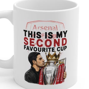 Op de afbeelding: Een witte keramische mok met een afbeelding van een persoon die een zilveren trofee kust. De tekst luidt Arsenal THIS IS MY SECOND FAVOURITE CUP. Het ontwerp bevat een rood Arsenal-embleem op de achtergrond en de Premier League-trofee.