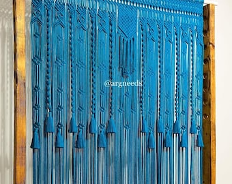 May include: A teal blue macrame wall hanging with a geometric pattern and tassels. The hanging is made of thick cord and is attached to a wooden frame.