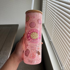 May include: Pink tumbler with a glittery finish and a design featuring a pastry and the text "Cafe con Pan"