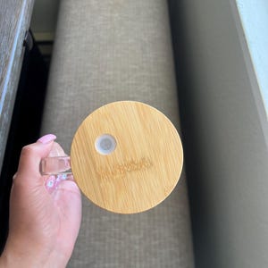 May include: A round, wooden lid with a small, white, circular opening in the center. The lid is made of light brown bamboo and has a smooth, polished finish.
