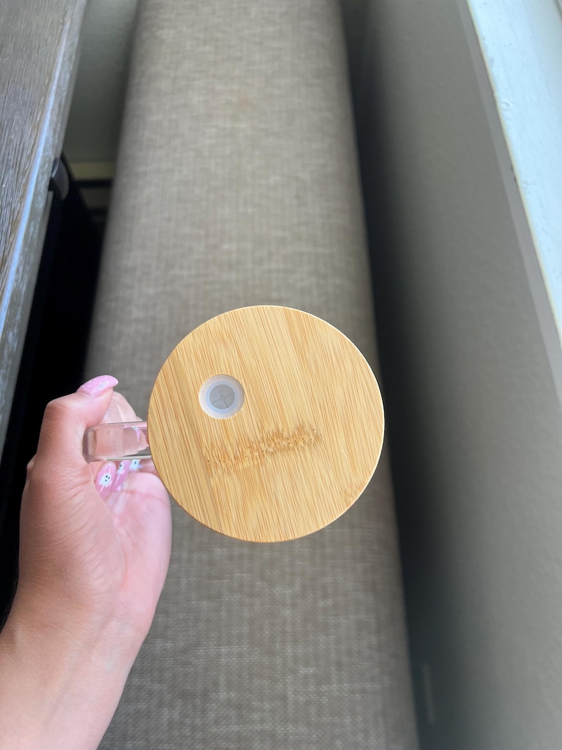 May include: A round, wooden lid with a small, white, circular opening in the center. The lid is made of light brown bamboo and has a smooth, polished finish.