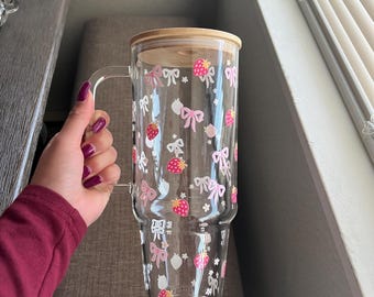 May include: A clear glass mug with a bamboo lid and a pink and white strawberry and bow pattern. The mug is double-walled and has a handle.