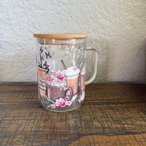 May include: A clear glass coffee mug with a bamboo lid, featuring a floral and coffee-themed design. The mug has a handle and is decorated with images of coffee drinks, flowers, and butterflies. The words "Coffee Please" are visible on the mug.
