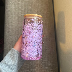 May include: A clear glass water bottle with a purple glitter design and a wooden lid.