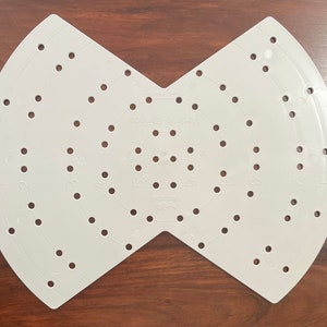 May include: A light grey plastic craft tool with numerous evenly spaced holes and curved edges. The tool is shaped like two semi-circles joined at a point. The text "Made in Canada" is visible.