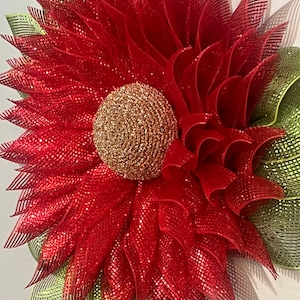 May include: A large, decorative flower wreath with a red, glittery mesh petal design. The center of the flower is a gold, glittery sphere. Green and gold striped mesh accents the outer edges of the flower.