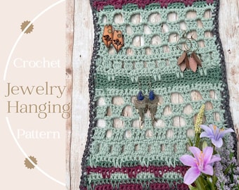 May include: Crocheted jewelry hanging pattern in shades of gray, green, and burgundy, with a wooden dowel for hanging. The pattern features a grid design with various earrings displayed. The text "Crochet Jewelry Hanging Pattern" is visible.