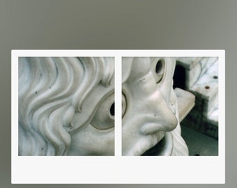 May include: Close-up of a white marble sculpture of a face with a large nose and a single eye. The sculpture is part of a larger piece, with only the face visible in the image. The sculpture is in a light gray background.