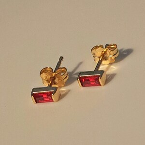 May include: A pair of gold stud earrings with a red rectangular gemstone.