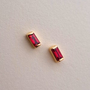 May include: A pair of gold stud earrings with red rectangular gemstones.