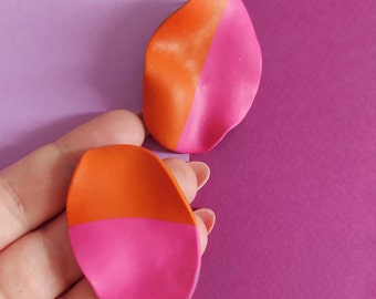 May include: A pair of handmade earrings with a unique, asymmetrical design. One earring is orange on top and pink on the bottom, while the other earring is pink on top and orange on the bottom.