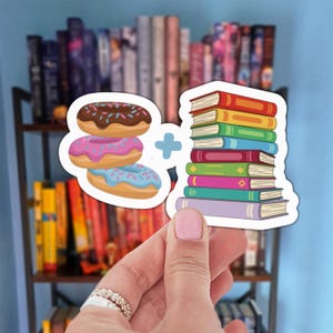 Puede incluir: Un diseño de pegatina con tres donuts con glaseado de chocolate, rosa y azul, combinados con una pila de libros coloridos. Los donuts y los libros están sobre un fondo blanco, con un signo más entre ellos.