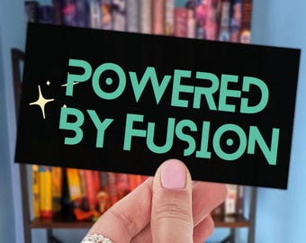 May include: A rectangular black sticker featuring the text POWERED BY FUSION in a bold, light teal sans-serif font. To the left of the text, there is a small, four-pointed star icon in a pale yellow color. The sticker has a smooth, matte finish.
