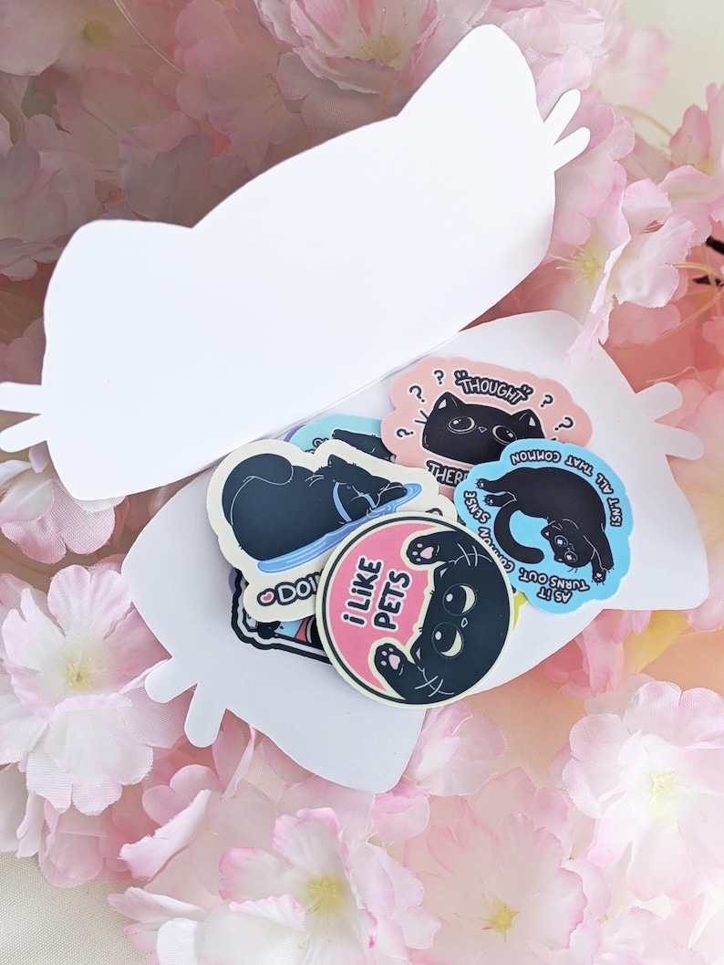 May include: A selection of cat-themed stickers in different shapes and colours. The stickers depict black cat illustrations with phrases such as "I like pets" and "Thought?" on a white cat-shaped card, surrounded by pink flowers.