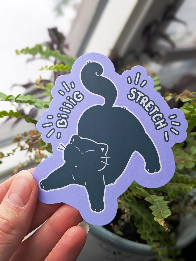 May include: A sticker showing a black cat stretching on a pale purple background. The sticker has the words "Biiiiig Stretch" in white, stylized text. The cat is in a relaxed pose, with its paws extended and tail curved.