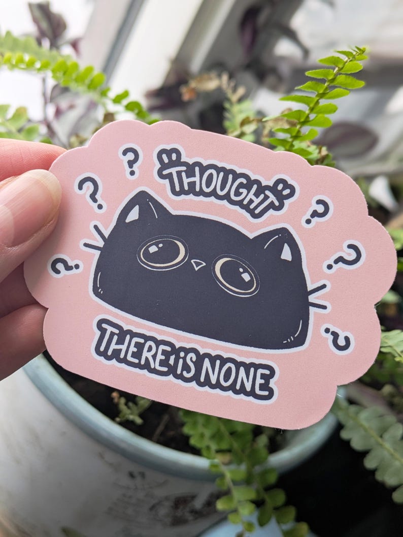 May include: A pink sticker featuring a black cat illustration and the text "THOUGHT THERE IS NONE." The cat has large eyes and question marks surround the cat's head. The sticker is held in front of a background of green plants.