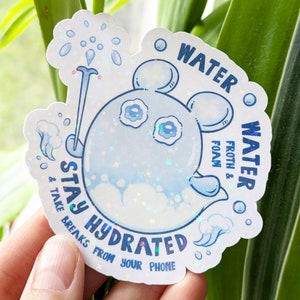 Puede incluir: Una pegatina holográfica con un personaje de dibujos animados azul y el texto "Stay Hydrated & Take Breaks From Your Phone." La pegatina también dice "Water Froth & Foam."