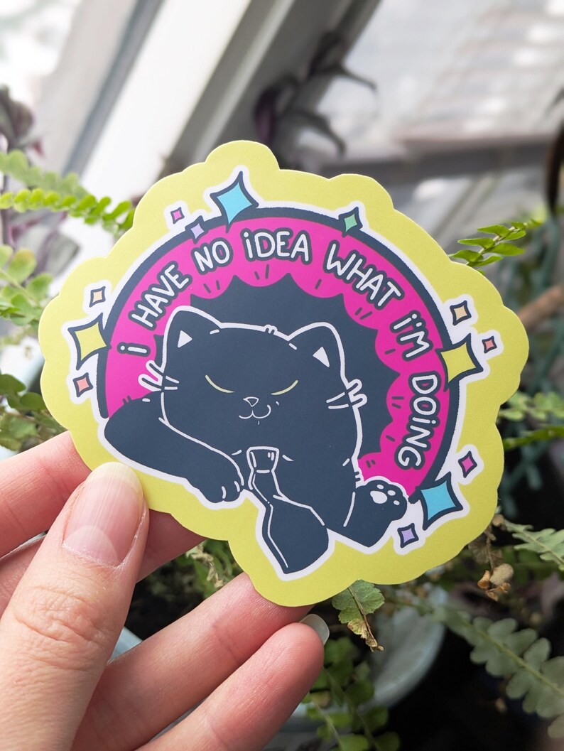 May include: A die-cut sticker featuring a black cat holding a bottle, with the text "I HAVE NO IDEA WHAT I'M DOING" in a pink and yellow design. The sticker has a yellow border with star and diamond accents.