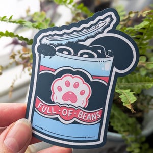 May include: A sticker depicting a cartoon can of beans with a cat paw print. The can is blue with a red stripe and the words "FULL OF BEANS" in white. The beans are black, and a cat paw is pink.