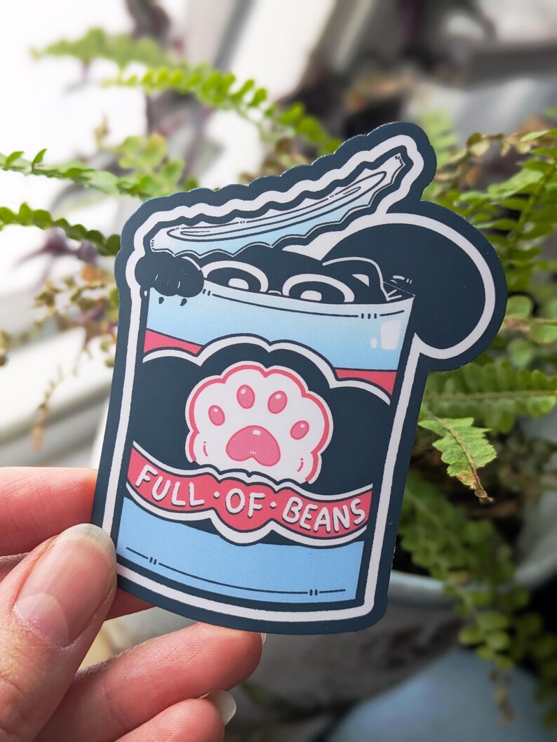 May include: A sticker depicting a cartoon can of beans with a cat paw print. The can is blue with a red stripe and the words "FULL OF BEANS" in white. The beans are black, and a cat paw is pink.