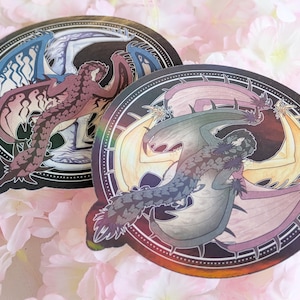 May include: Two round stickers with a black background and a circular design. Each sticker features a colorful, detailed illustration of a dragon with wings spread out. The dragon on the left sticker is red and orange, while the dragon on the right sticker is green and blue.