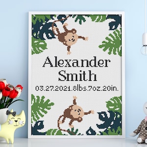 May include: A white framed cross-stitch with a jungle theme. It features two brown monkeys, green leaves, and the text "Alexander Smith 03.27.2021 8lbs 7oz 20in."