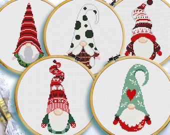 May include: Five embroidered Christmas gnomes in different colors and patterns, each in a wooden embroidery hoop. The gnomes are wearing red, green, white, and black hats with different designs.
