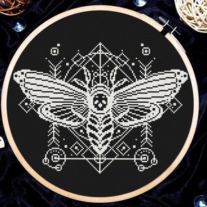 Può includere: Ricamo a punto croce in bianco e nero con un motivo di falena con motivi geometrici su uno sfondo nero.