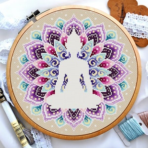May include: A cross-stitch embroidery hoop with a colorful mandala design featuring a silhouette of a person meditating in the center. The mandala is in shades of purple, pink, blue, and yellow.