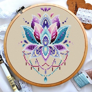 May include: A cross-stitch embroidery hoop featuring a colourful floral design. The design includes a large flower with purple, pink, blue and yellow accents. The flower is surrounded by a geometric pattern.