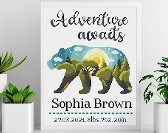 May include: A white framed cross-stitch design featuring a bear silhouette with a forest scene inside. The text "Adventure awaits" is above the bear and "Sophia Brown" is below the bear. The date "27.03.2021" and the weight and length "8lbs 7oz 20in" are below the name.